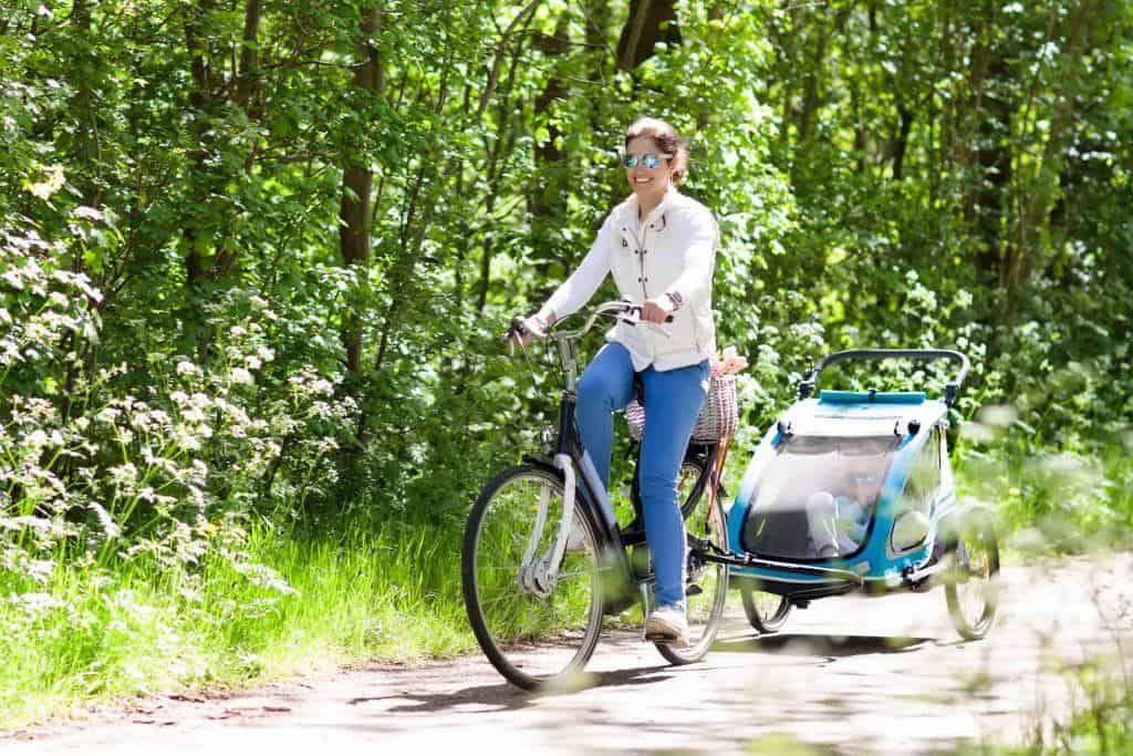 Mother on bicycle with baby bike trailer in park