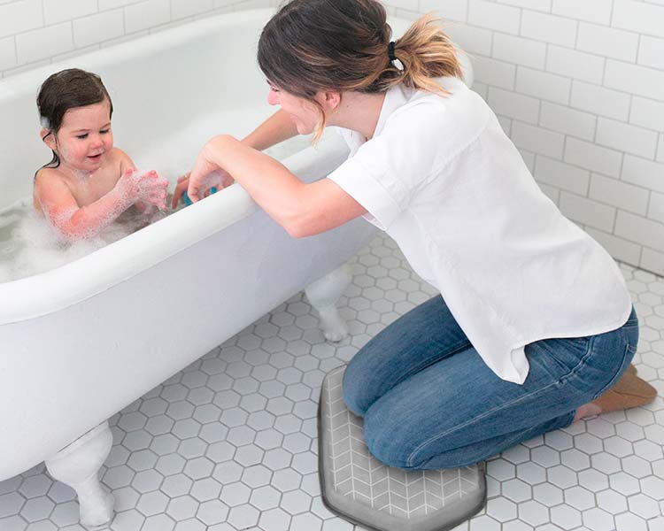 Mom resting knees on bath kneeler while baby is in bath tub