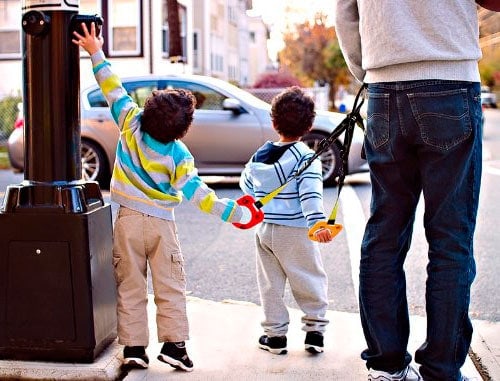 two children holding a walking handle on a busy street