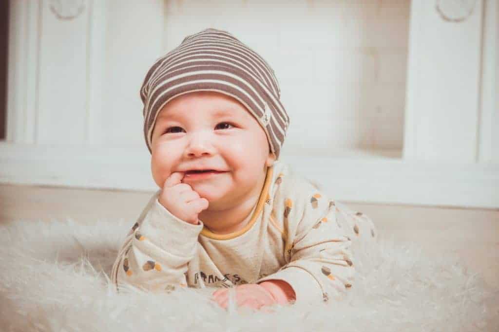 Smiling baby biting right index finger
