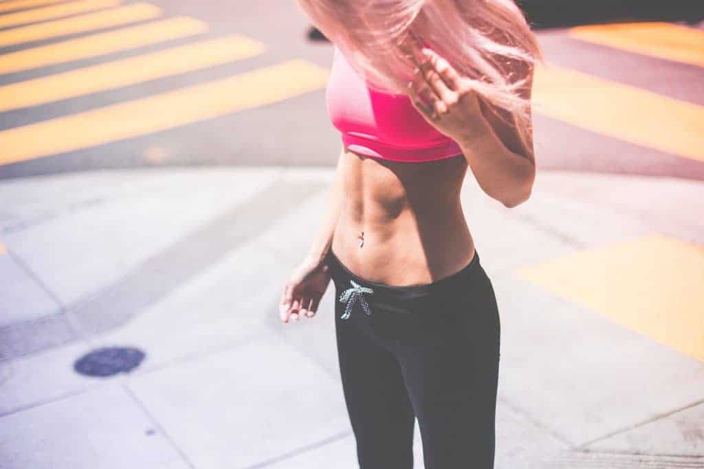Woman is looking at her abs and she is wearing a pink push up bra and leggings