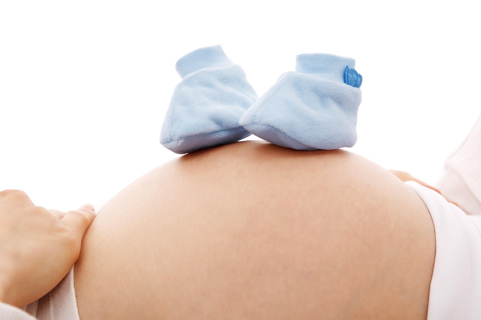 Tummy of a pregnant women and a pair of baby shoes on top of it