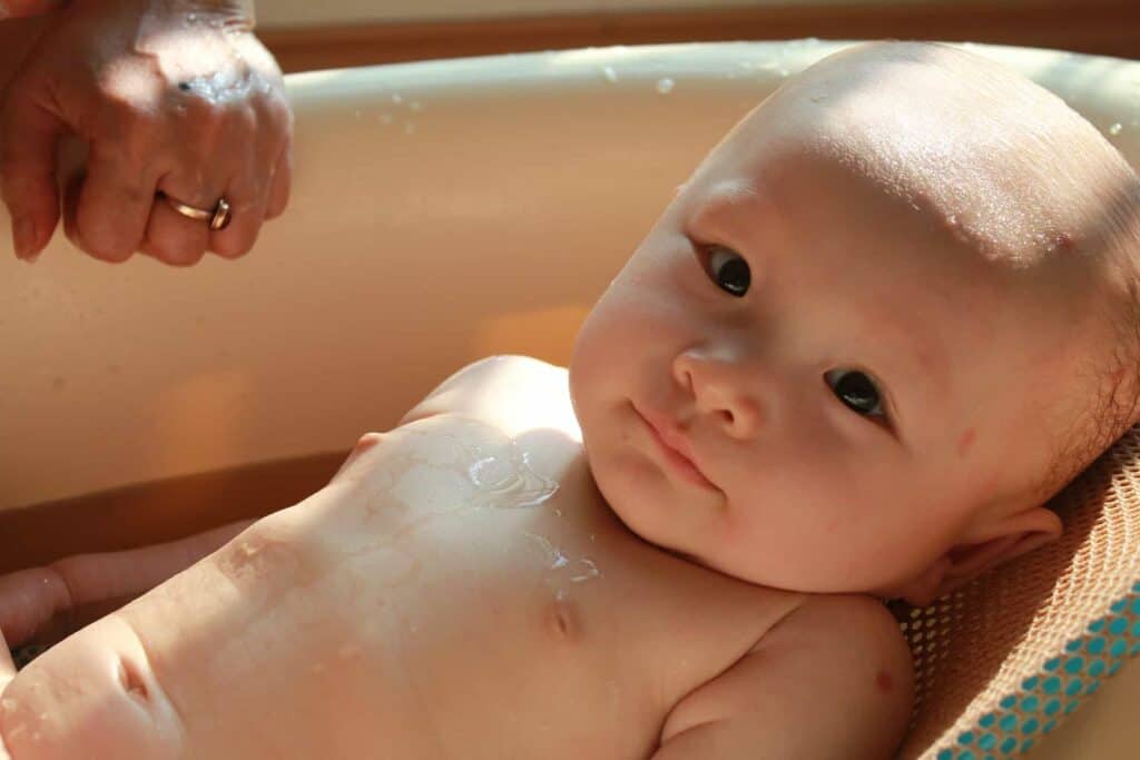 A baby in an infant tub having his hair washed with the best baby shampoo