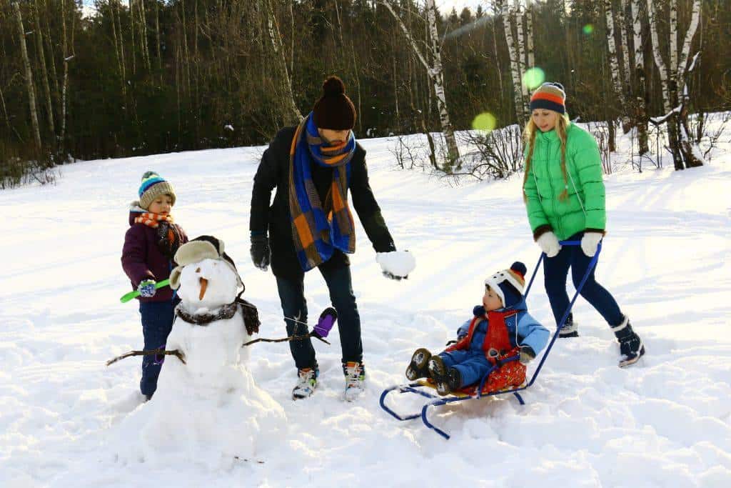 Family playing and building a snow man while their 2 boys is wearing the best toddler snow boots