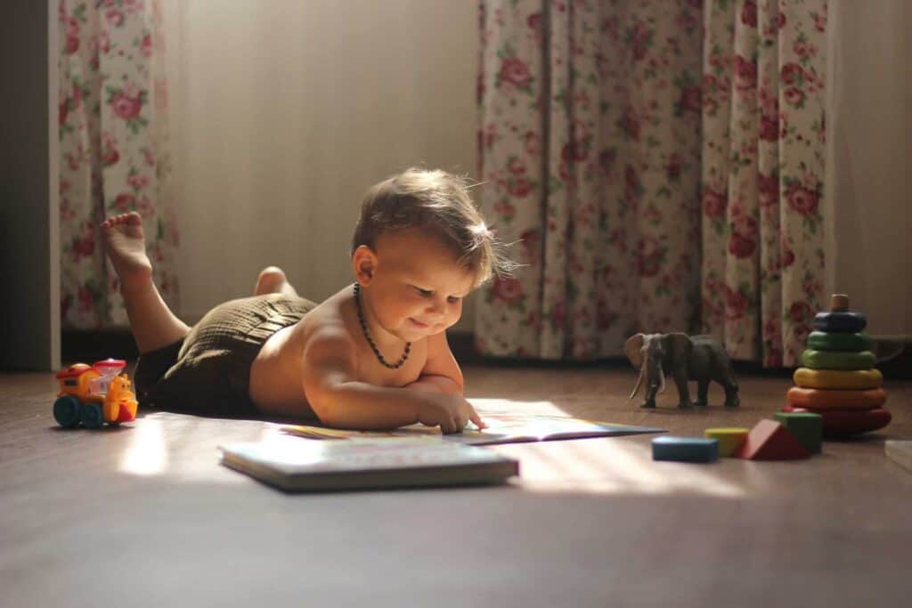 A baby with cabin fever entertains himself by playing on the floor with a book