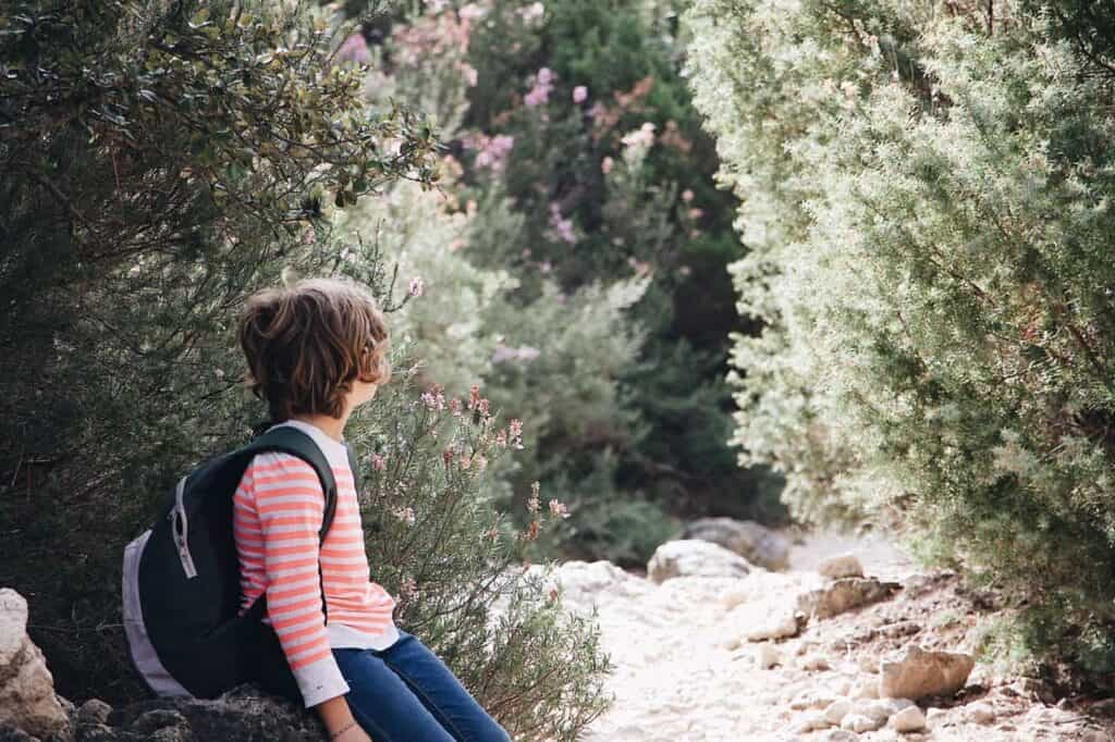 boy wearing red and white striped sweater sitting on rock