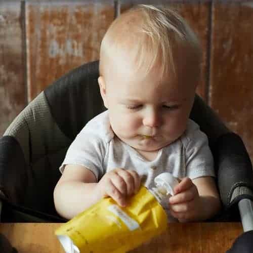 baby sitting on chair holding yellow soft-tube