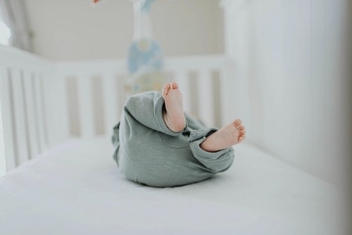 baby lying insede a crib wearing gray pants