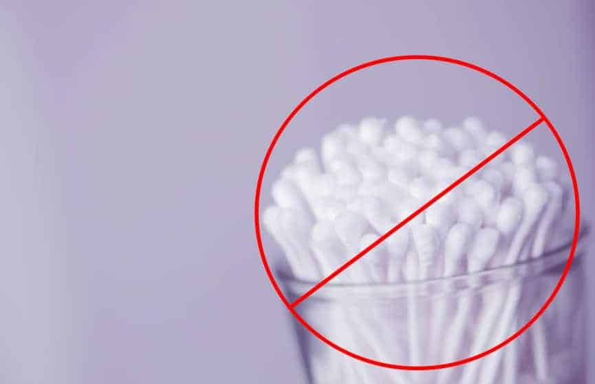 a lilac background with a container of cotton ear swabs in the foreground with a red circle and slash for "no" over them.
