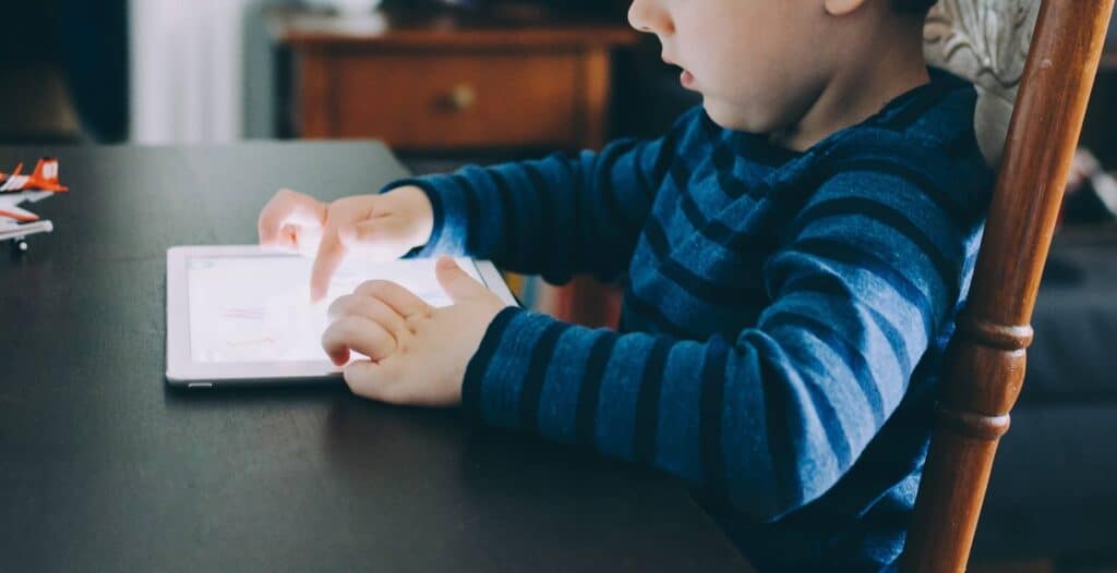 A boy sitting at a table to use the LeapFrog Epic Academy Edition app on his tablet.