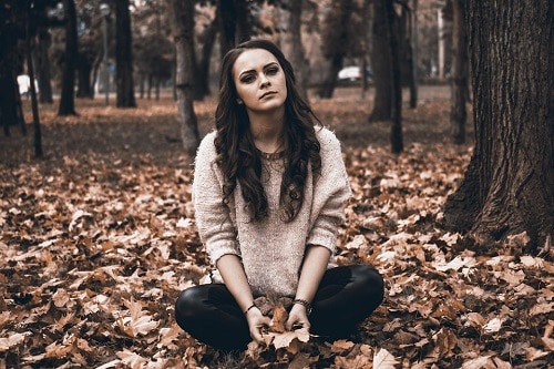 sad woman sat on ground full of leaves