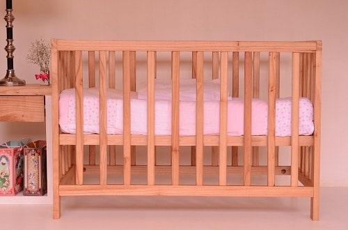 wooden crib with pink baby sheet