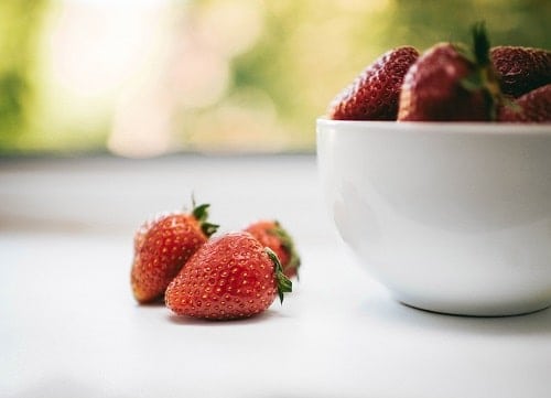 three red strawberries beside bowl with strawberries