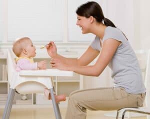 baby sitting in high chair being fed baby food by mom