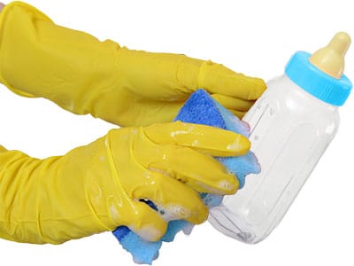 two hands in rubber gloves washing a baby bottle with a soapy sponge