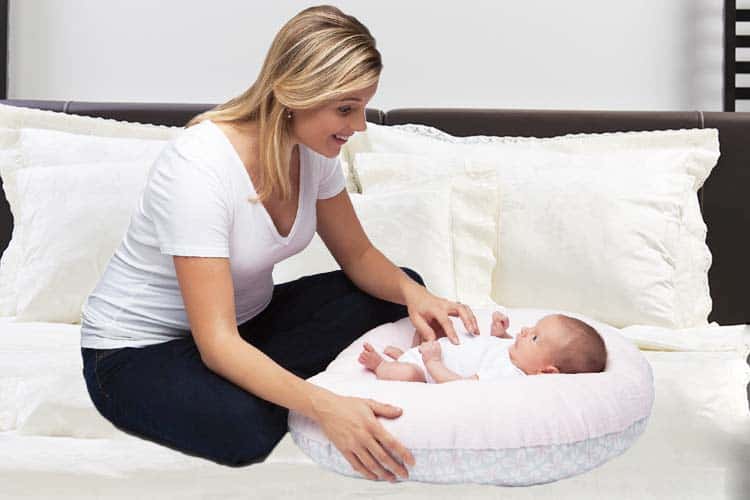 Woman playing with baby in lounger on bed