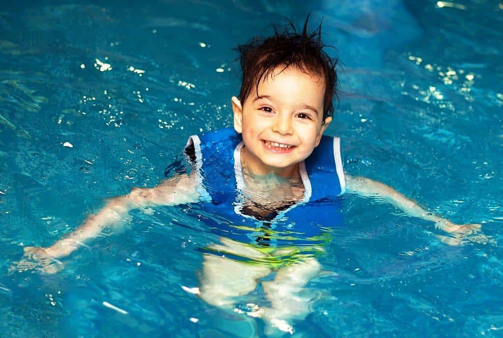 Young boy with inflatable swimming vest in the pool, has a happy