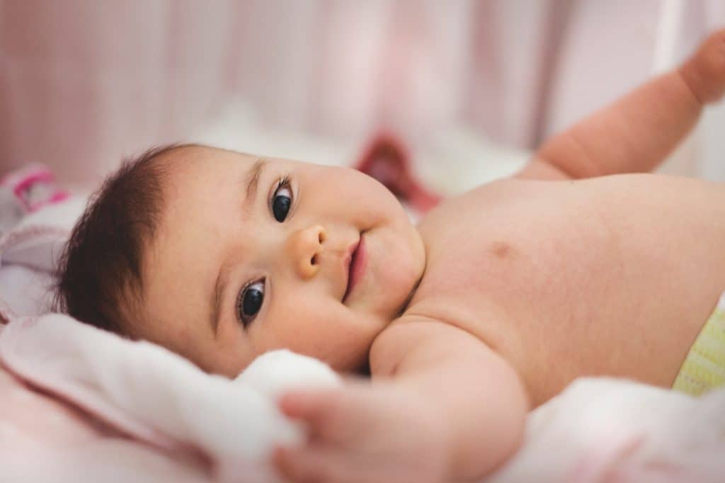 Baby lying and smiling on pink bed