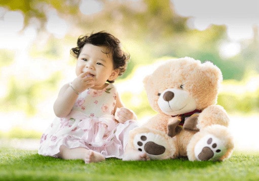 toddler sitting on a grass with brown teddy bear