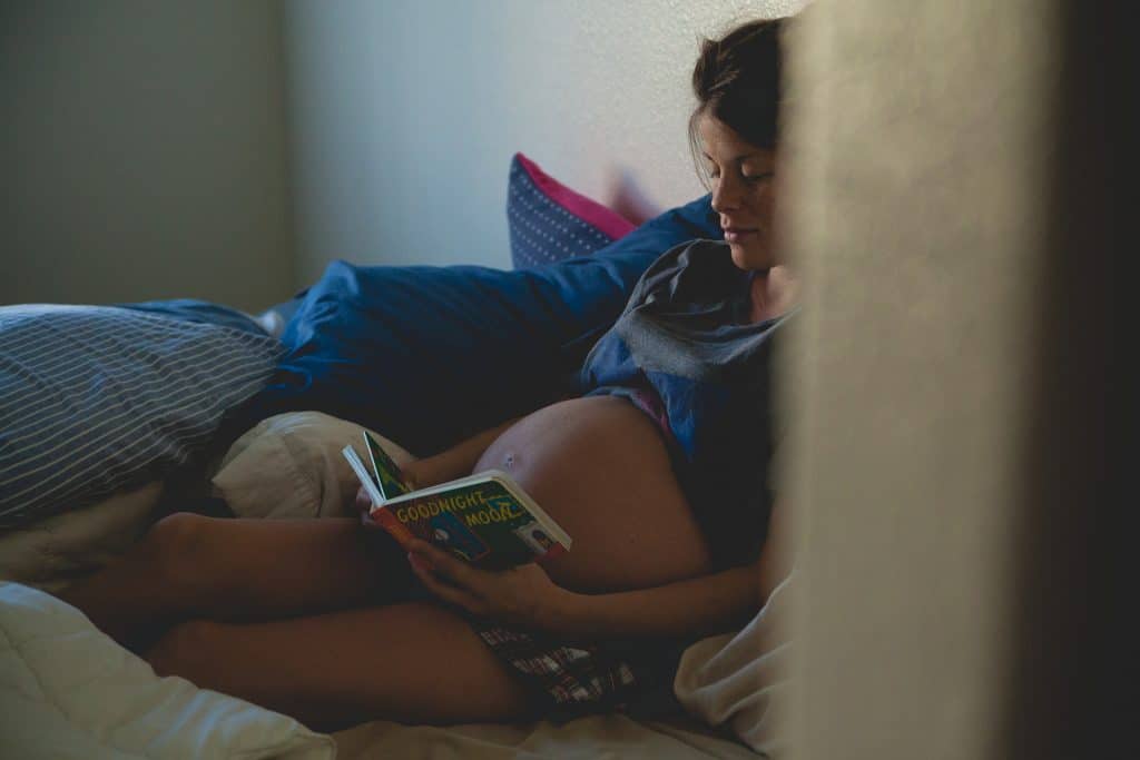 Pregnant Woman is reading a book while lying on bed