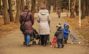 2 mothers holding a stroller while walking at the park with their children
