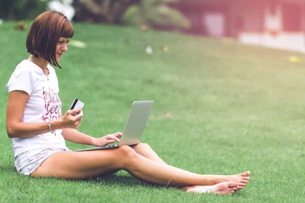 woman holding a card and a laptop while sitting on the grass