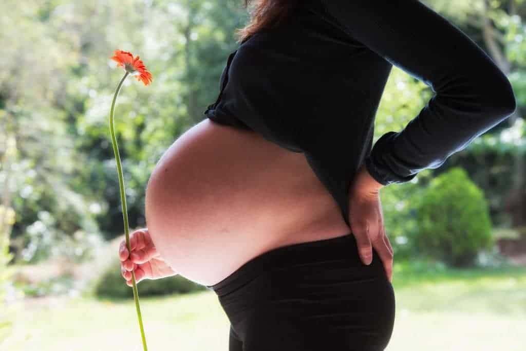 Pregnant women is holding a flower while wearing a black sleeve and the best maternity leggings
