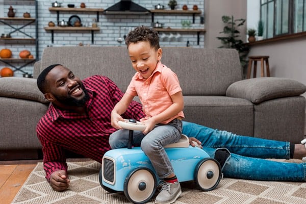 Black boy driving toy car with father