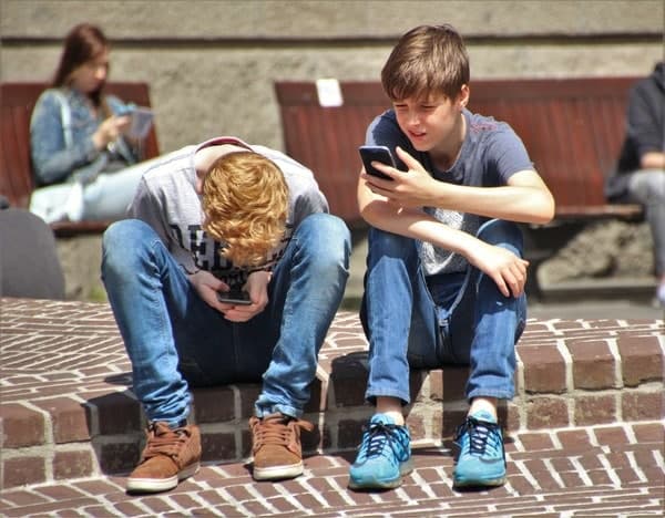 2 Boy Sitting On Brown Floor While Using Their Smartphone