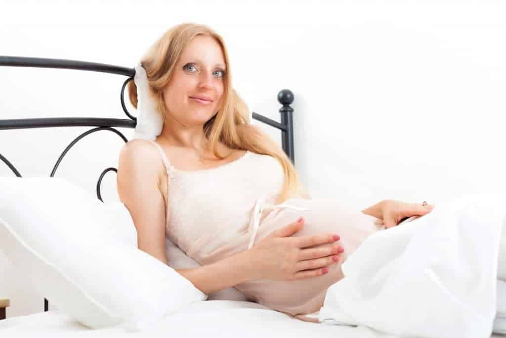 Blonde cute pregnant woman on white pillow in bed