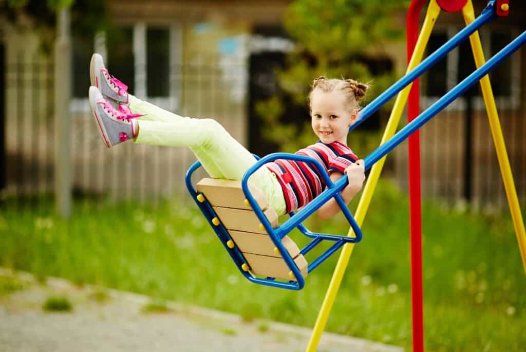 Happy little girl looking at camera while swinging on playground area