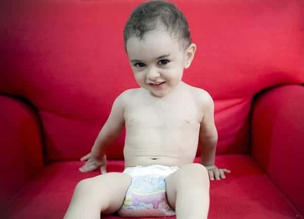 baby sitting on red sofa and wearing diaper.