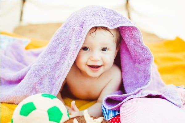 toddler boy lying covered with purple towel