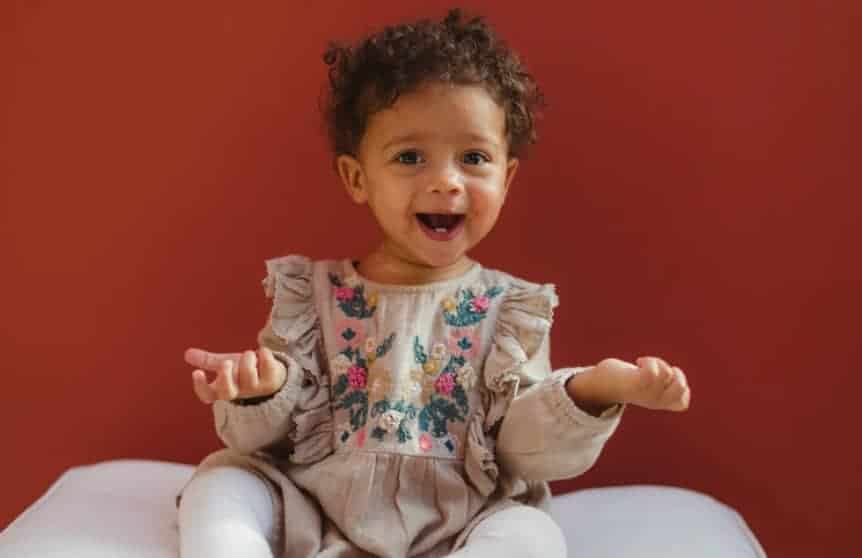 baby girl makes questioning gesture with big smile on a red background
